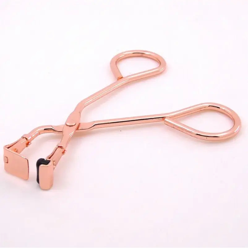 Rose gold eyelash curler with scissor-like handles.