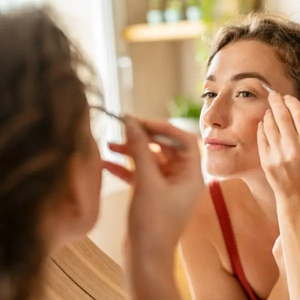 Woman applying makeup to her face in a bathroom mirror.