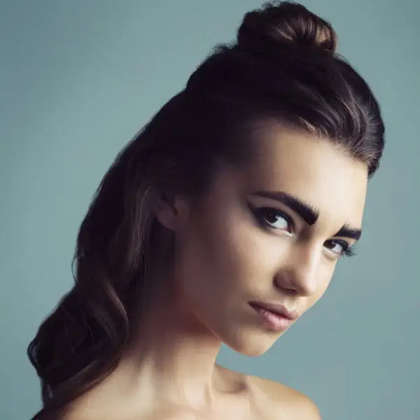 Young woman with dark hair styled in a high bun and loose waves, gazing intently at the camera.