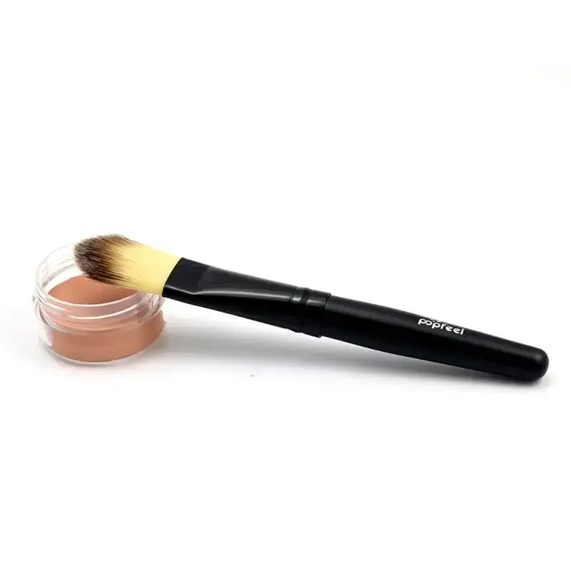 Makeup brush with black handle next to an open container of powder or foundation.