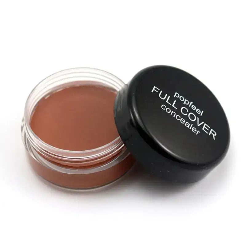 Open jar of brown concealer makeup with a black lid labeled ’Full Cover concealer’.