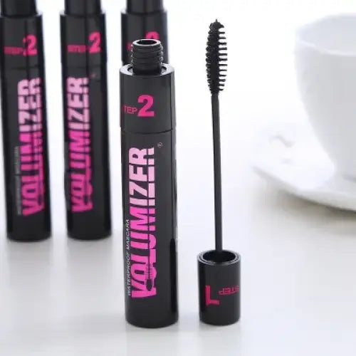 Black mascara tube with pink ’Volumizer’ text and an open wand applicator.