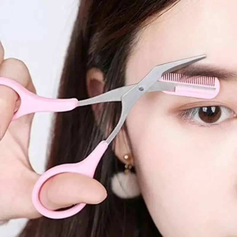 Pink-handled eyebrow trimming scissors with a built-in comb attachment.