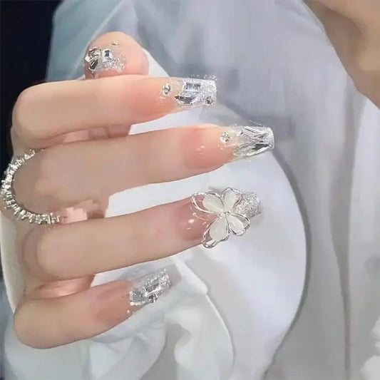 Hand with long, ornate acrylic nails and a butterfly-shaped ring.