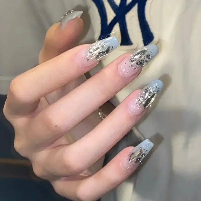 Hand with long, ornate acrylic nails featuring a glittery silver and white design.