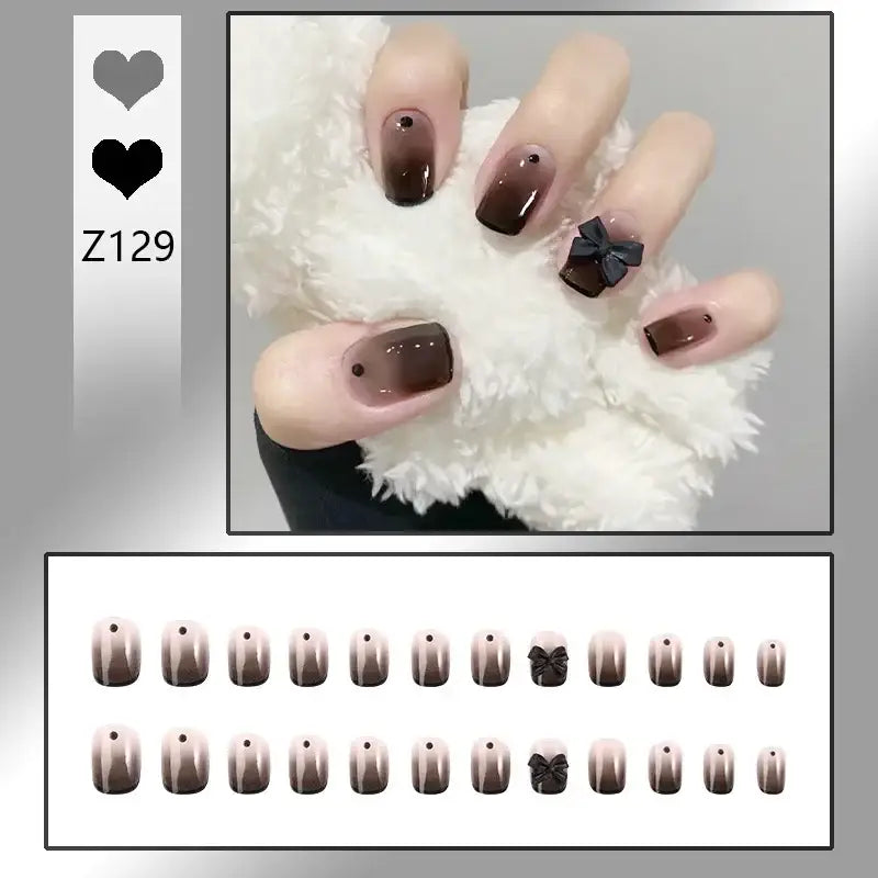 Hand with manicured nails featuring a brown ombre design and black bow accent.