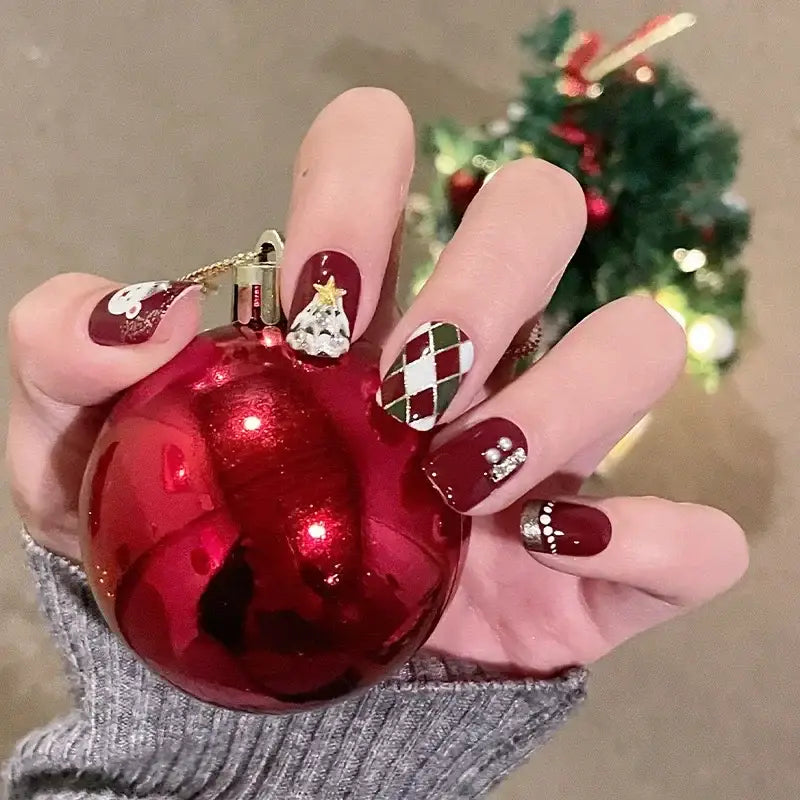 Hand holding a shiny red Christmas ornament, showcasing festive nail art designs.