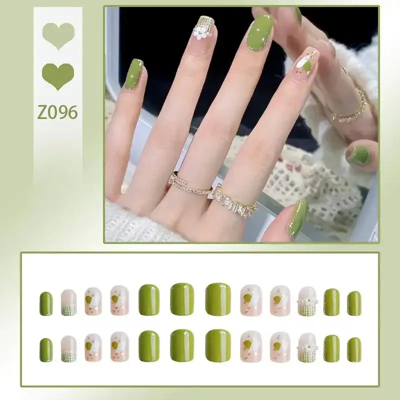 Manicured hand with green and white nail designs and delicate rings.