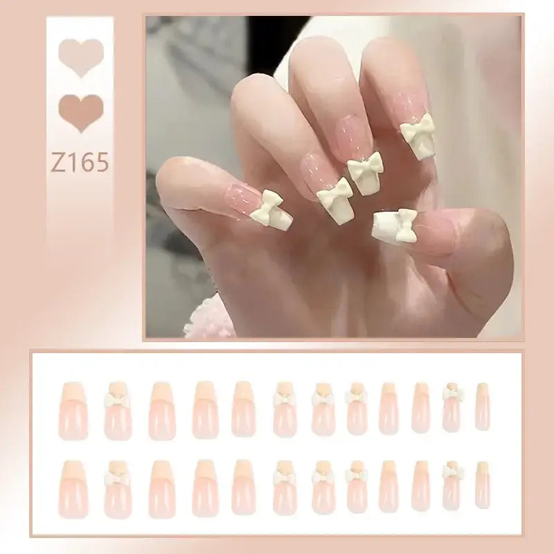 Manicured hand with pale pink nails and white bow decorations on the tips.