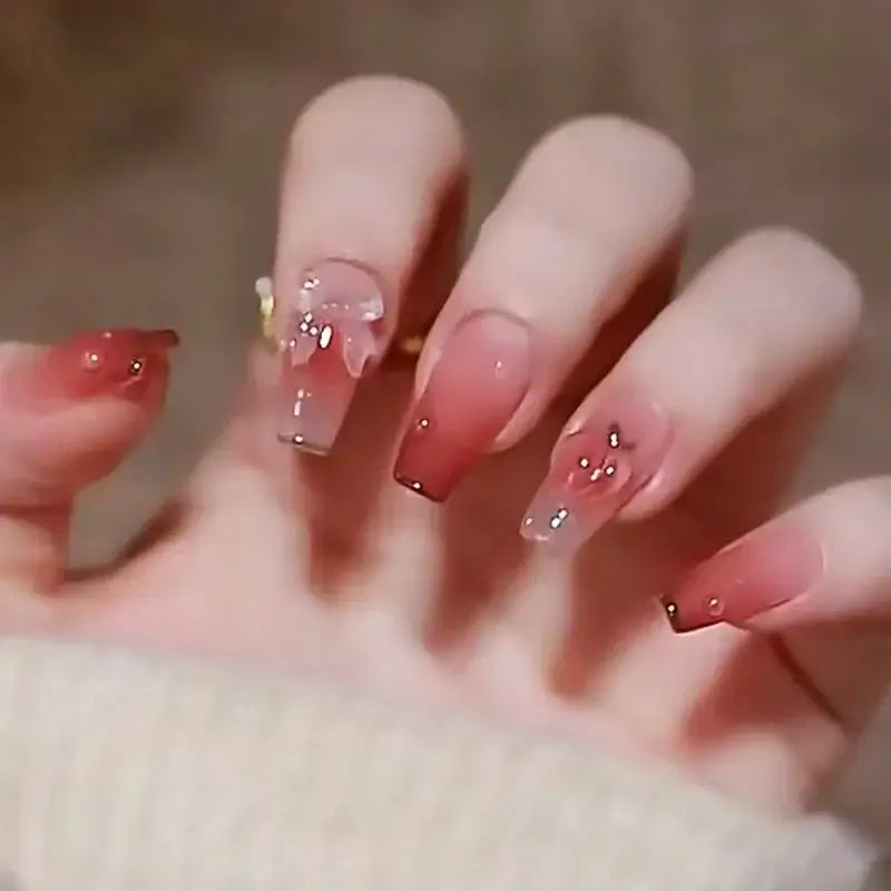 Manicured hand with long, pink ombré acrylic nails adorned with glitter and rhinestones.