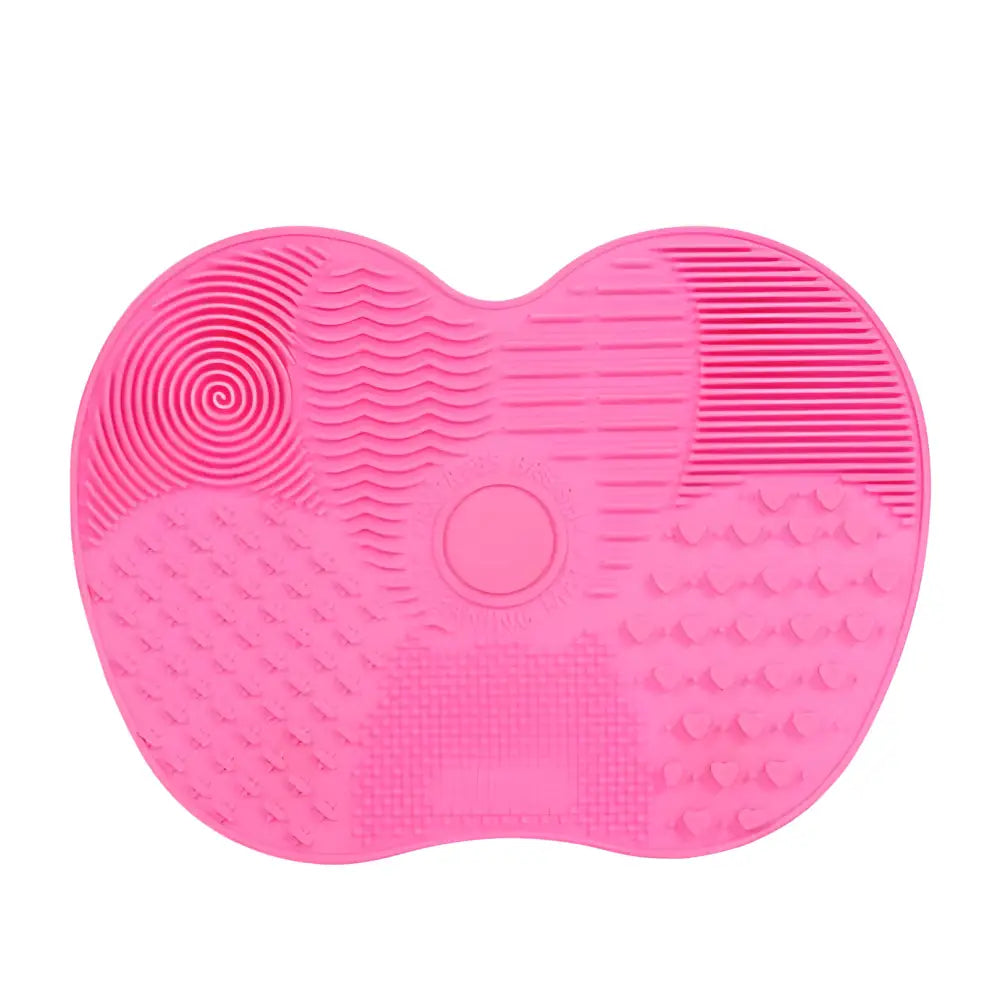 Pink heart-shaped silicone brush cleaning mat with various textured sections.