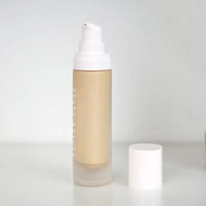 Frosted glass bottle containing beige liquid cosmetic product with a white pump dispenser.