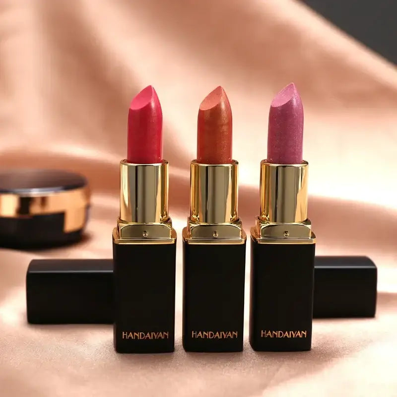 Three lipsticks in gold and black tubes standing upright.