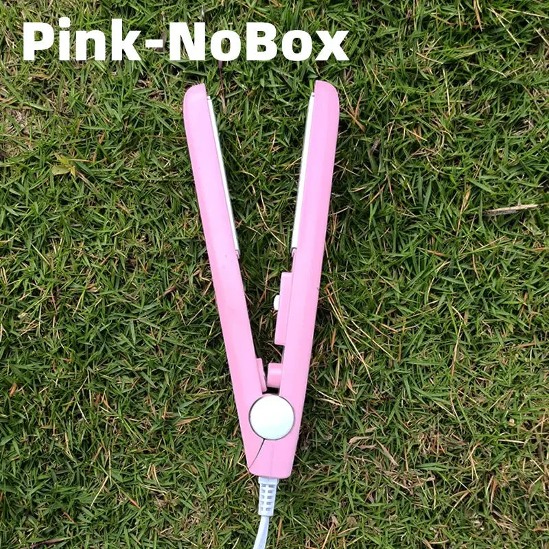 Pink hair straightener or flat iron lying on grass.