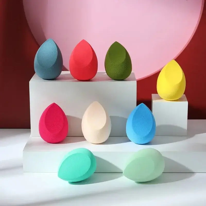 Colorful teardrop-shaped makeup sponges arranged on geometric platforms.