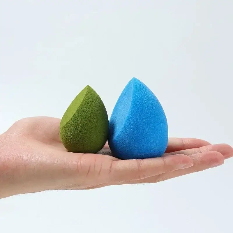 Two teardrop-shaped makeup sponges, one green and one blue, resting on an open palm.