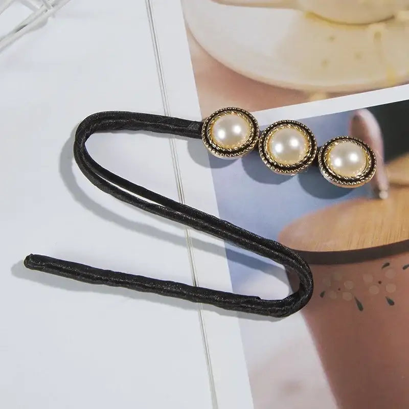 Hair clip with three pearl-like decorative elements on a black elastic band.