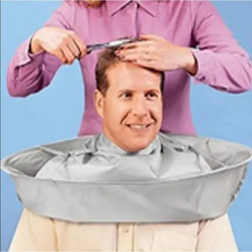 Smiling man wearing a gray hair-cutting cape while someone trims his hair.