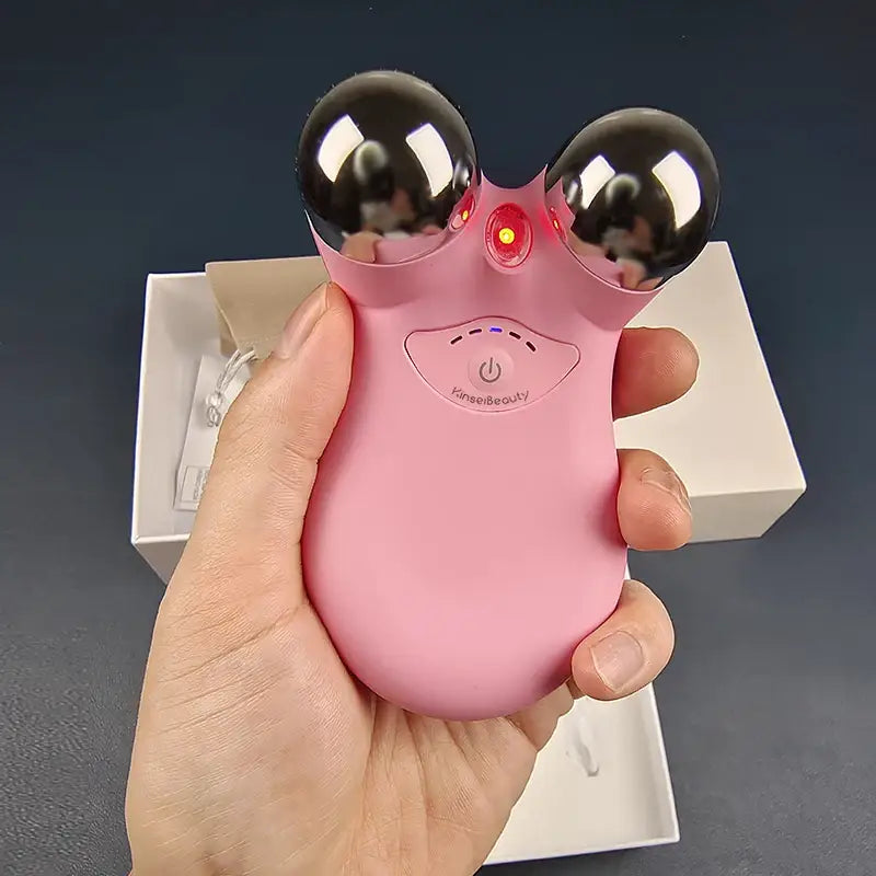 Pink handheld device with two metallic spheres and a cartoon face design.