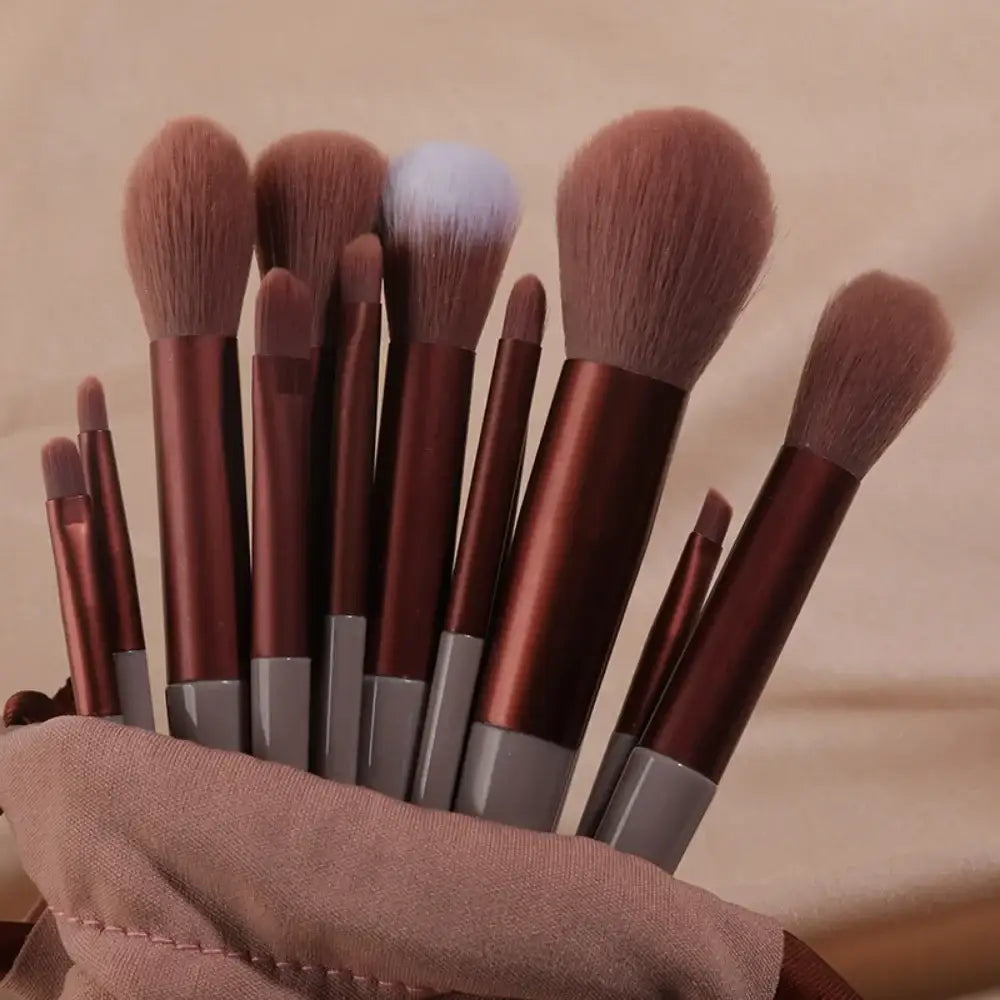 Set of makeup brushes with brown handles in a fabric holder.