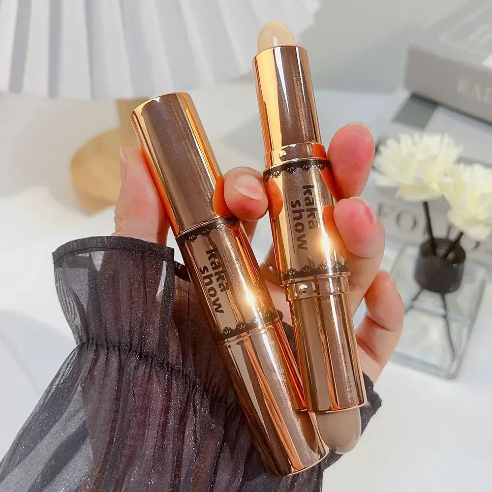 Gold-colored makeup concealer sticks held in a hand.