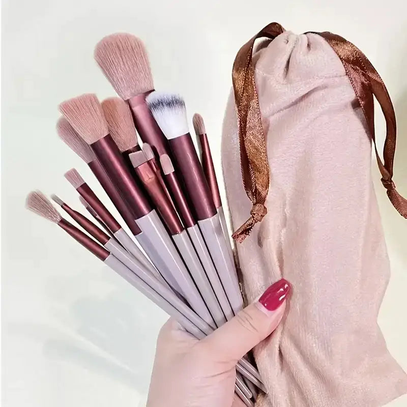 Set of makeup brushes with pink and white handles held in a hand with red nail polish.