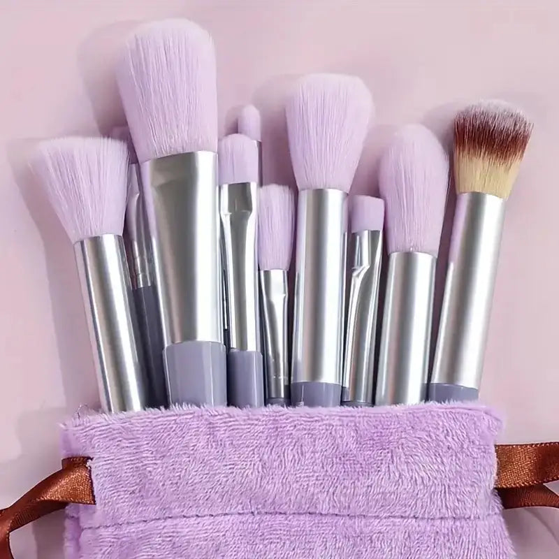 Set of makeup brushes with silver handles and mostly lavender bristles in a purple fuzzy holder.