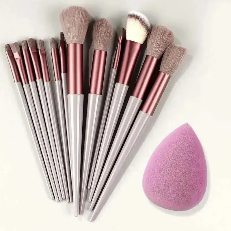 Set of makeup brushes with white handles and rose gold ferrules, accompanied by a pink beauty blender sponge.