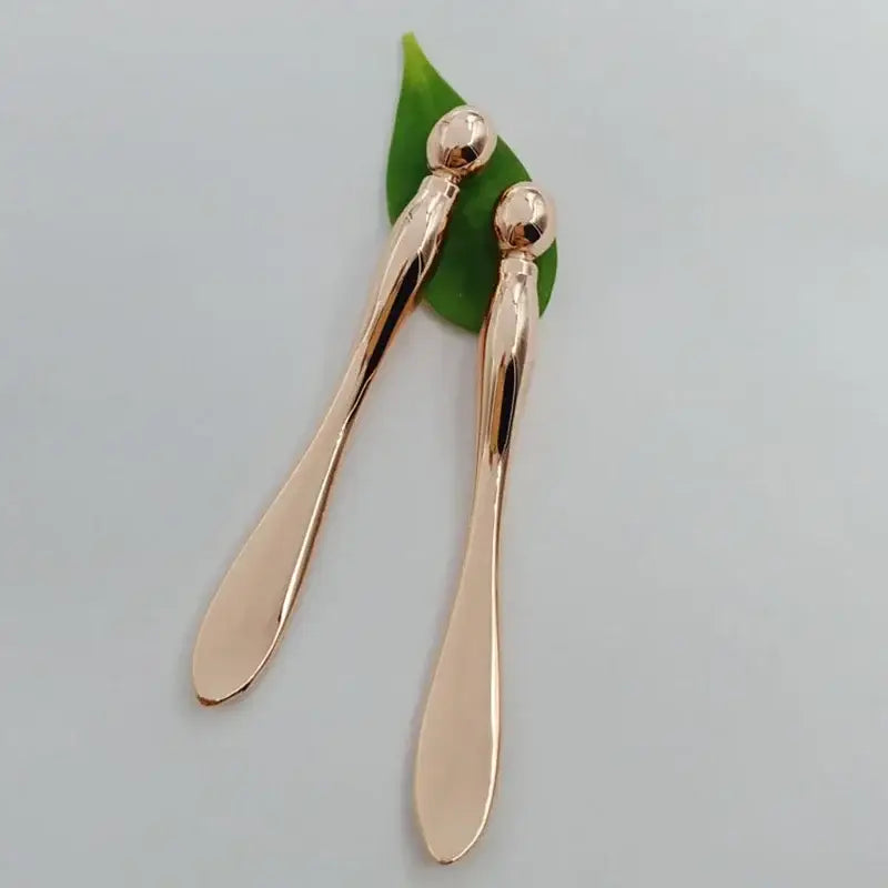 Pair of elongated gold-colored metal spoons with rounded handles.