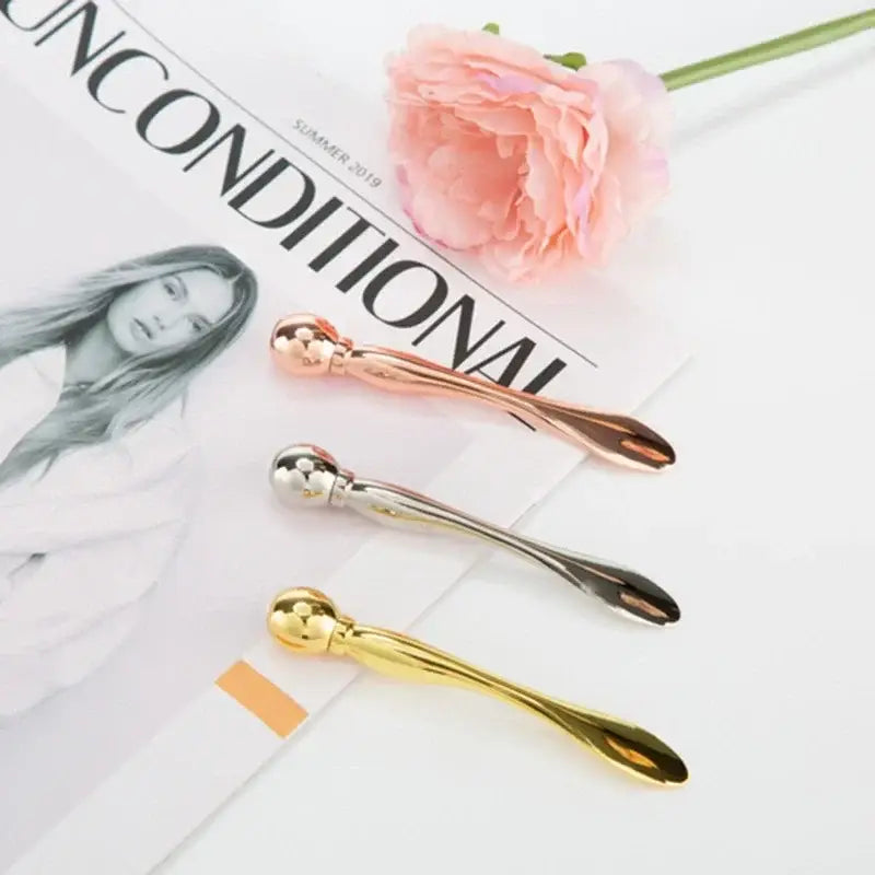 Three metallic spoon-shaped facial massage tools in gold, silver, and rose gold colors.