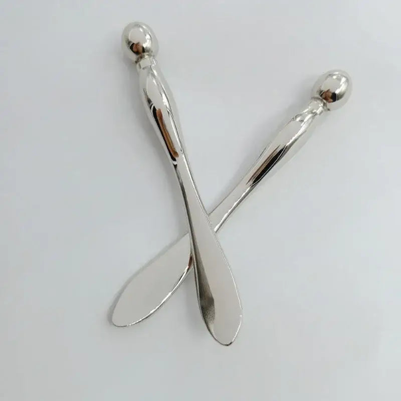 Two crossed silver spoons with elongated handles and round finials.