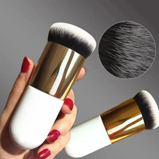 Makeup brush with a white handle and gold metallic ferrule held by a hand with red nail polish.