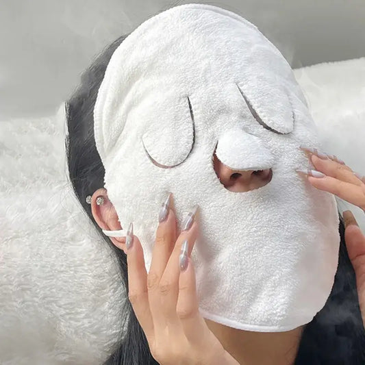 White plush face mask with cartoon-like closed eyes being applied to a person’s face.